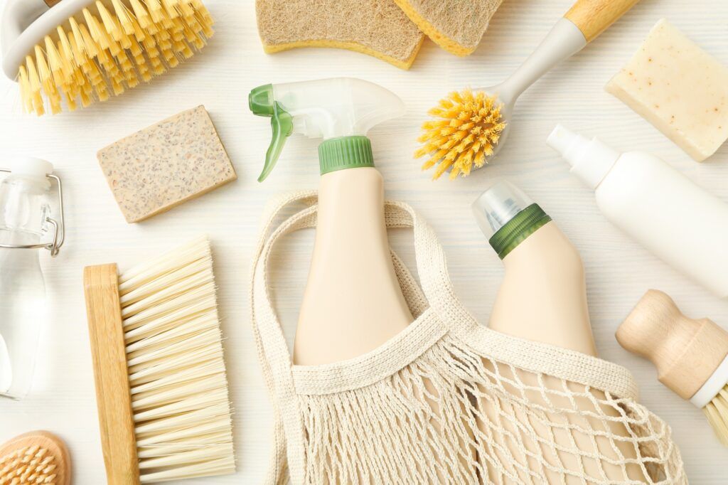 Eco bag, bottles with detergents and cleaning tools on light background, top view